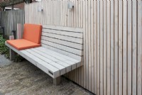 Banc en bois spécialement conçu à la clôture en bois avec coussins orange. Éclairage à la clôture.