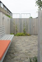 Clôture en bois avec grimpeurs au patio. Banc en bois spécialement conçu à la clôture en bois avec coussins orange. Éclairage à la clôture.