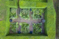 Vue sur petit jardin formel contenu par des haies d'ifs taillés ; image prise avec un drone. Allées de briques et parterres rectangulaires contenus par des garde-corps Juillet. L'été.