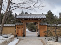 Photo d'hiver de l'entrée d'un jardin japonais avec des portes traditionnelles de style pergola. Mur de pierre, rochers et pin sculptural en premier plan