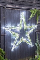 Étoile en bois avec guirlandes lumineuses et brins de cèdre sur mur en bois noir