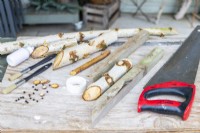 Bâtons de bouleau, scie, grains de poivre, ruban de masquage et pinceaux disposés sur une surface en bois