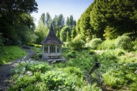 Pavillon à côté du ruisseau bordé d'hostas, de primevères et de fougères dans le jardin de la tourbière à l'ancien presbytère, Netherbury, Dorset en mai
