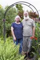 Couple debout sous arche dans leur jardin en août.