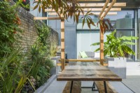 Vue d'une cour-jardin contemporaine avec pergola, table de pique-nique et terrasse, grandes jardinières et plantes d'aspect tropical. septembre