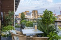 Une table à manger sur un balcon bordé de jardinières de romarin, de laurier, d'olivier, de palmier, de graminées ornementales, de marguerites, de némésias et de pétunias.