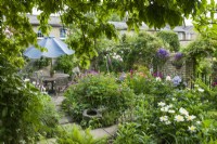 Vue d'une partie de la salle à manger isolée dans le jardin de la ville en été avec des roses et des plantes vivaces herbacées, y compris des pivoines, des géraniums et des digitales. Juin