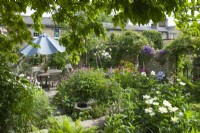 Vue sur la salle à manger dans un jardin de ville isolé en été avec des roses et des plantes vivaces herbacées, notamment des pivoines, des géraniums et des digitales. Juin