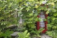 La reine dans une cabine téléphonique rouge dans la folie - un coin salon ombragé au jardin de Hamilton House en mai