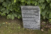 Une ardoise recyclée porte une citation sur le jardinage et est affichée à côté d'une haie de hêtres. Lewis Cottage, jardin NGS Devon. Le printemps.