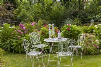 Coin salon au parterre d'hortensias avec hortensias de jardin, lys à crête, Hydrangea quercifolia 'Snowflake'. Meubles de style de vie en métal peint en blanc table chaises pelouse.