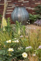 Une urne en bronze dans un patio-jardin contemporain, avec un parterre de fleurs à thème doré contenant Anemanthele lessoniana, Rosa 'Tottering by Gently' et Pimpinella major 'Rosea'
