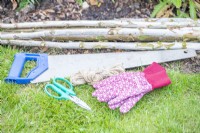 Scie, ciseaux, ficelle, gants et bâtons de bouleau disposés au sol