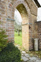 Ouverture dans un mur de briques menant à un verger dans un jardin de campagne