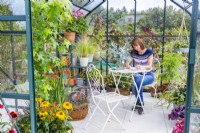Femme assise à table écrit dans une serre remplie de diverses plantes et pots
