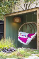 Salon de lecture extérieur avec banc en bois suspendu à côté des parterres de fleurs avec Heuchère 'Marmelade de Citron vert' et lumière