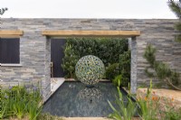 Mur revêtu de pierre offrant une vue sur une pièce d'eau Geminus par David Harber, Camassia et Iris en avant-plan - Une évasion paisible, RHS Malvern Spring Festival 2022