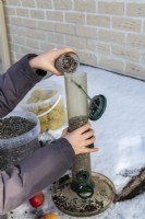 Enfant remplissant une mangeoire à oiseaux avec des graines de tournesol le jour de la neige en hiver