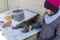 Enfant remplissant une mangeoire à oiseaux en métal avec des graines de tournesol