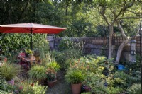Petit jardin de ville de style cottage construit en pensant à la faune, un grand parasol orange fournit de l'ombre et des pots recouvrent le patio pavé