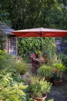 Petit jardin de ville de style cottage construit en pensant à la faune, un grand parasol orange fournit de l'ombre et des pots recouvrent le patio pavé