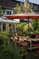 Petit jardin de style cottage de ville construit avec la faune à l'esprit, grand parasol orange fournit de l'ombre sur la table et les chaises de jardin