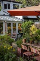 Petit jardin de style cottage de ville construit avec la faune à l'esprit, grand parasol orange fournit de l'ombre sur la table et les chaises de jardin