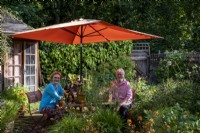 Les propriétaires de jardin assis sous un parasol dans un jardin de cottage de Londres, l'été