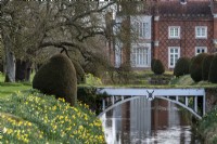 Un pont sur les douves qui entoure le jardin clos à Helmingham Hall. Au printemps les ifs taillés, les cônes de Taxus baccata sont entourés de jonquilles.