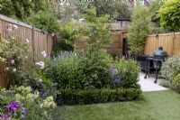 Jardin de banlieue isolé avec pelouse artificielle, parterre de fleurs herbacées et clôture en bois contemporaine.