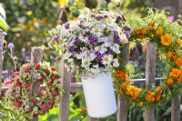 Bouquet de verveine, d'achillea et de marguerites dans un pot en émail et une couronne faite d'hortensias et de fruits Cornus kousa accrochés à une clôture.