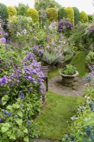 Zone en contrebas d'un jardin de curé avec des parterres à thème de couleur et une urne de verveines pourpres en juillet