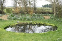 Vue d'ensemble de l'étang rond du jardin printanier et des parterres de fleurs remplis de crocus et de perce-neige.