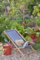Chaise longue sur gravier et parterre de fleurs surélevé avec cultures en croissance dans le potager.