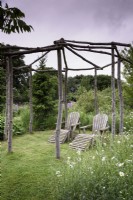 Une paire de fauteuils inclinables en bois sous une tonnelle rustique en mai