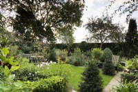 Jardin champêtre en septembre avec un mélange de conifères taillés, de vivaces et de plantes tendres comme les pélargoniums en pots.
