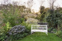 Banc blanc entouré d'arbustes et d'arbres au jardin de John Massey en octobre.