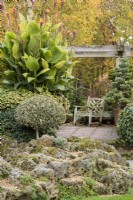 Terrasse entourée de houx taillés et d'un paysage alpin rocheux au jardin de John Massey en octobre.