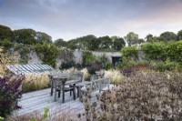Salon de terrasse en bois avec des sièges encadrés par Eryngium alpinum et Stipa tenuissima à Whitburgh Walled Garden en septembre