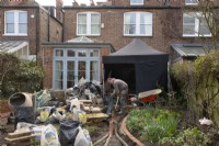 Des matériaux de construction et un ouvrier au début du relooking d'un petit jardin londonien.