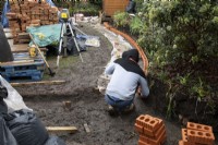 Un ouvrier construisant un muret de briques autour d'un parterre de fleurs surélevé lors de la rénovation d'un petit jardin londonien.