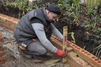 Un ouvrier construisant un muret de briques autour d'un parterre de fleurs surélevé lors de la rénovation d'un petit jardin londonien.