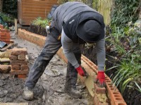 Un maçon construisant un muret autour d'un parterre surélevé lors de la rénovation d'un petit jardin londonien.