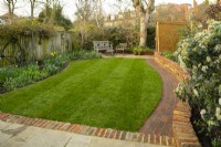 Une 'photo d'après' d'un petit jardin londonien après une cure de jouvence qui comprenait un nouveau muret de briques, un chemin incurvé, une terrasse étendue et un gazon nouvellement posé.