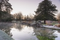 Étang avec brume et réflexions en janvier dans le jardin du palais épiscopal, Wells, Somerset