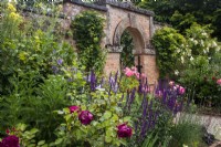 L'été dans le potager à Morton Hall Gardens avec un parterre mixte contre le mur de briques avec une arche derrière. Rosa 'Falstaff' et 'Boscobel'.
