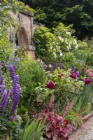 Parterre de fleurs mixtes d'été dans le potager à Morton Hall avec des lupins, des heuchères, des roses et des delphiniums et une arche dans un mur de briques derrière..