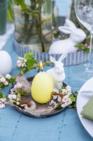 Bougie en forme d'œuf avec des œufs plus petits, des plumes, des fleurs et une figure de lapin comme décorations de Pâques