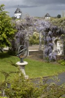 Un cadran solaire armillaire sur socle avec pergola couverte de glycines derrière. Trago Mills montrent les jardins, Devon, Royaume-Uni. Peut. Printemps