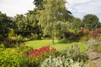 North House Garden avec parterres de fleurs vivaces entourant une pelouse circulaire; Monarda 'Gardenview Scarlet' au premier plan